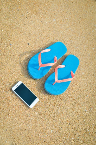 Vista superior de cerca en el teléfono móvil con zapatillas en el fondo de la playa de verano. Felices vacaciones alegres — Foto de Stock