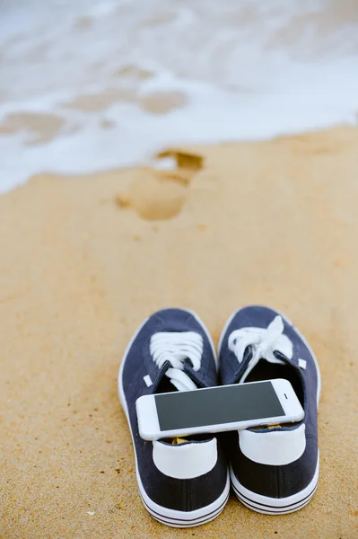 Vista superior no telefone móvel com tênis em fundo de praia de verão arenoso. Feche-se, férias alegres felizes — Fotografia de Stock