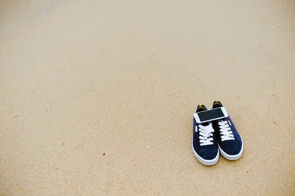Προβολή επάνω στο κινητό τηλέφωνο με πάνινα παπούτσια σε φόντο αμμώδης καλοκαίρι παραλία. Εσωτερικη, ευτυχισμένη χαρούμενη διακοπές — Φωτογραφία Αρχείου