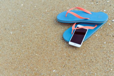 Üstten Görünüm üstünde hareket eden telefon ile terlik yaz plaj zemin üzerine kapatın. Mutlu neşeli tatil