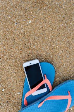 Üstten Görünüm üstünde hareket eden telefon ile terlik yaz plaj zemin üzerine kapatın. Mutlu neşeli tatil