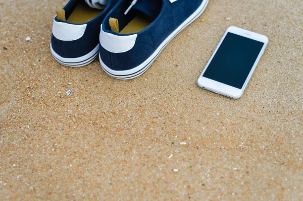 Vista superior no telefone móvel com tênis em fundo de praia de verão arenoso. Feche-se, férias alegres felizes — Fotografia de Stock