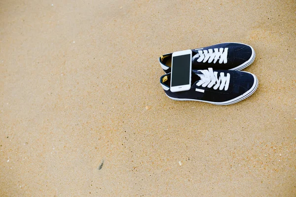 Προβολή επάνω στο κινητό τηλέφωνο με πάνινα παπούτσια σε φόντο αμμώδης καλοκαίρι παραλία. Εσωτερικη, ευτυχισμένη χαρούμενη διακοπές — Φωτογραφία Αρχείου