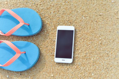 Üstten Görünüm yakın çekim yaz plaj arka plan üzerinde cep telefonu flip flop üzerinde. Mutlu neşeli tatil