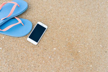 Üstten Görünüm üstünde hareket eden telefon ile terlik yaz plaj zemin üzerine kapatın. Mutlu neşeli tatil