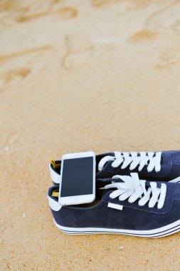 Kumlu yaz plaj arka plan üzerinde ayakkabı ile üstten görünüm üstünde hareket eden telefon. Yakın, mutlu neşeli tatil