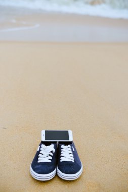 Kumlu yaz plaj arka plan üzerinde ayakkabı ile üstten görünüm üstünde hareket eden telefon. Yakın, mutlu neşeli tatil