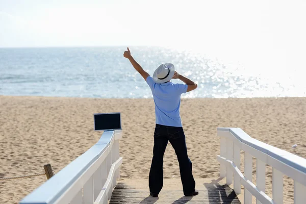 Emocionado hombre ocupado trabajando en el portátil y hablando en el móvil. Hombre en sombrero hablando en teléfono inteligente sobre el cielo azul y el fondo del océano — Foto de Stock