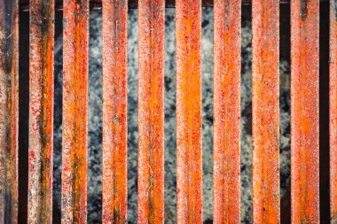 Dikey parmaklıkları ve turuncu aşınması olan paslı eski bir metal ızgaranın ayrıntılı makro dokusu. Tasarım, doku örtüleri veya inşaat kavramları için mükemmel endüstriyel arkaplan.