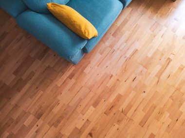 Turkuaz mavi kanepesi ve parlak ahşap zeminde sarı bir minderi olan rahat bir oturma odasının üst manzarası. Minimalist ve şık iç tasarım konsepti