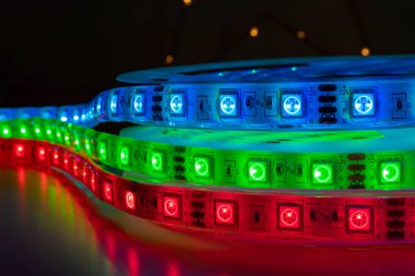 Elektronik bileşenleri, dirençleri ve 12V işaretlerini gösteren RGB LED ışık şeritlerinin makro yakın çekimi. Elektronik, DIY projeleri, akıllı ışıklandırma sistemleri ve Arduino meraklıları için teknoloji ışıklandırma arka planı.