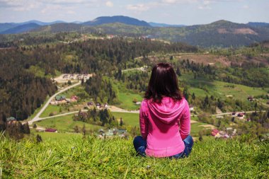 genç kız bir tepe üzerinde oturur ve dağlara görünüyor