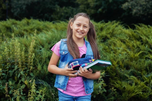 Красивая маленькая девочка, стоящая во дворе с книгами и блокнотами — стоковое фото