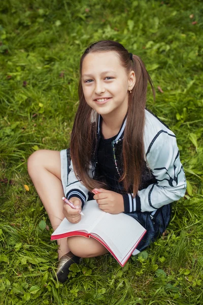 Usmívající se malá školačka psaní v poznámkovém bloku — Stock fotografie