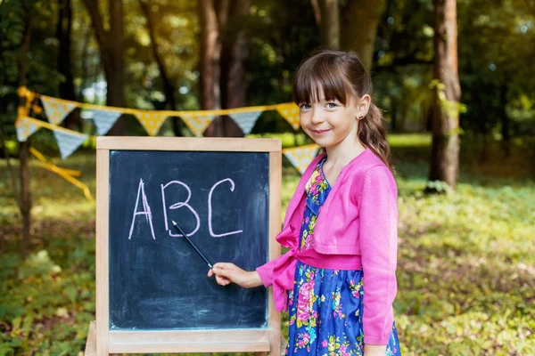 Una niña inteligente enseña en la junta de ABC. Concepto de aprendizaje y escuela — Foto de Stock