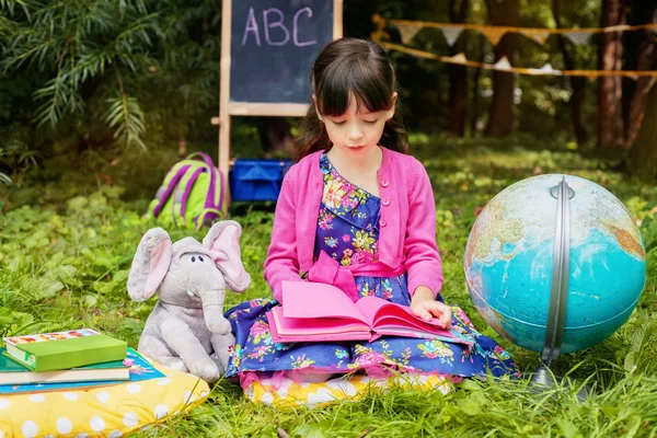 Lilla vackra flicka i en klänning som läser en bok — Stockfoto