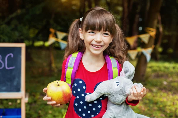 Gelukkig mooi meisje schoolmeisje met een appel en een olifant. Het concept van school en onderwijs — Stockfoto