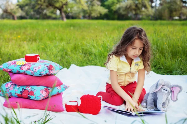 Malá holčička, čtení knihy v parku — Stock fotografie