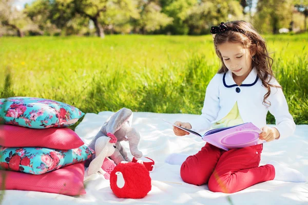 Schönes kleines Mädchen liest ein Buch im Park — Stockfoto
