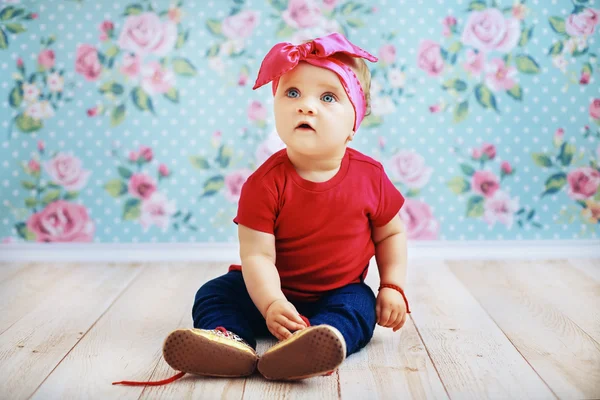 Beautiful baby in a pink jacket and jeans sitting on the floor.