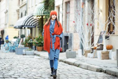 a girl with long hair in a coat and a red scarf walks around the city, walking along the Christmas shops and shop Windows, walking along the old streets. clipart