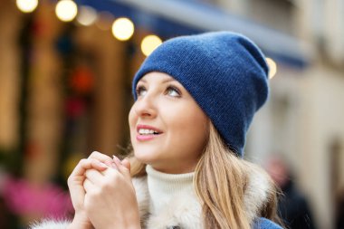 Eşarplı ve şapkalı genç bir kız Noel şehrinde yürürken ellerini ısıtıyor.
