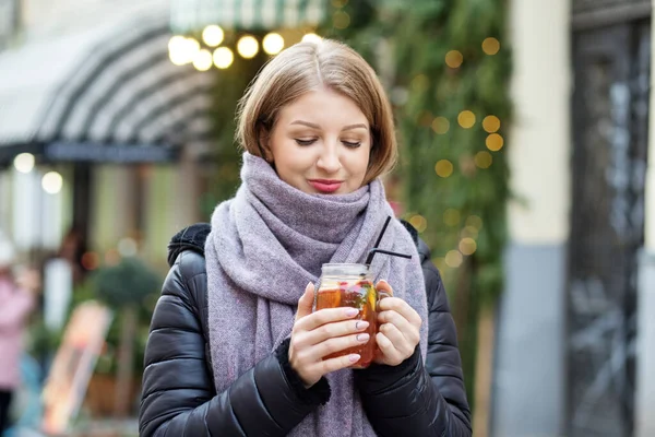 スカーフと帽子の少女が路上で熱い飲み物を飲んでいる クリスマス街を歩き 熱いお茶を手に入れましょう クリスマスセール — ストック写真