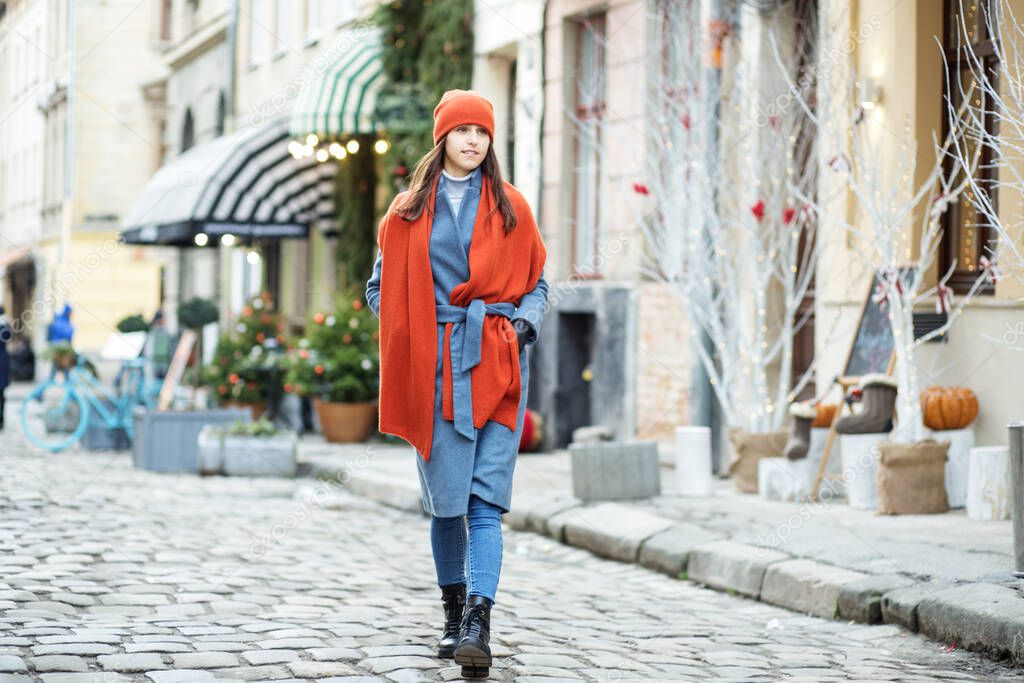 a girl with long hair in a coat and a red scarf walks around the city, walking along the Christmas shops and shop Windows, walking along the old streets.