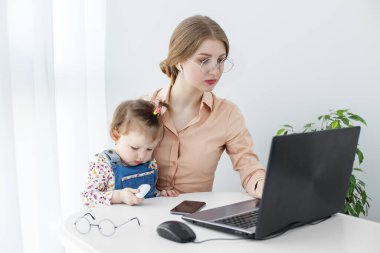 Genç bir kadın evde dizüstü bilgisayar kullanarak çalışıyor. Küçük bir çocuk annesinin yanında oturuyor. Doğum izninde çalış. Küçük kız annesinin yanında oynuyor..