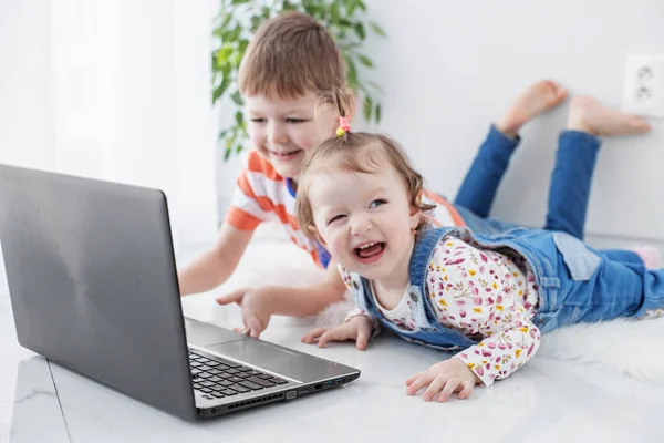 Small children watch funny videos on a laptop. Lie on the floor. Family, childhood, internet and games concept