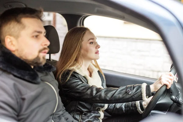 A girl and a man are sitting in a black car, a girl is driving, a good driver, learning to drive. The concept of a business woman, a girl learning to drive