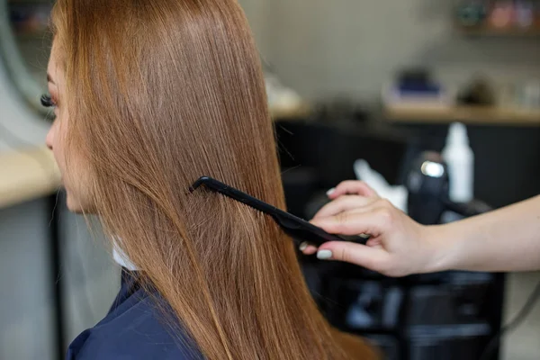 A woman in a barber shop combs her long hair.