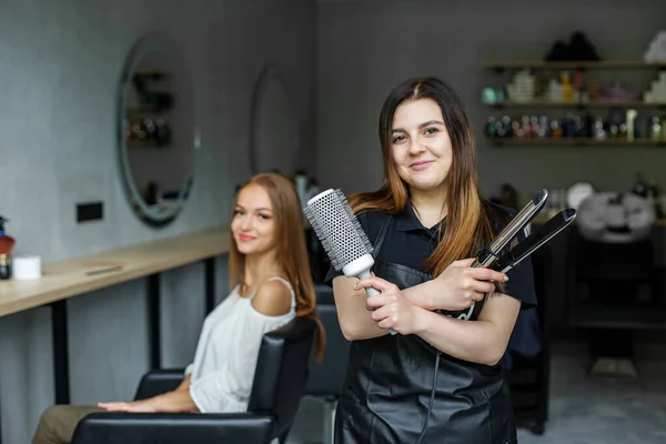 Fryzjer trzyma szczotkę i żelazo, aby wyprostować włosy. Klient siedzi na krześle.. — Zdjęcie stockowe