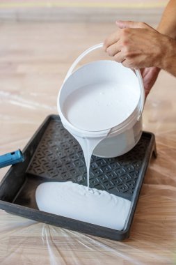 Tabladaki boya silindirini kapat. Beyaz boyayla dolu boya tepsisinin yakın görüntüsü. Ressam ve dekorasyon için araçlar