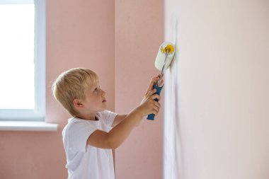 Ev tadilatı. Genç çocuk boya silindiriyle iç duvarı boyuyor..