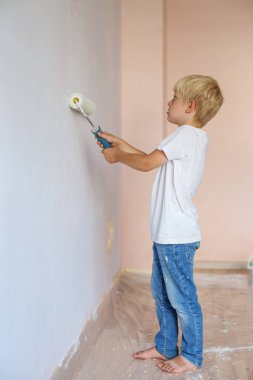 Ev tadilatı. Genç çocuk boya silindiriyle iç duvarı boyuyor..