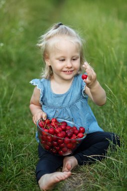 Küçük kız kiraz yiyor. Doğa manzarası. Organik yiyecekler
