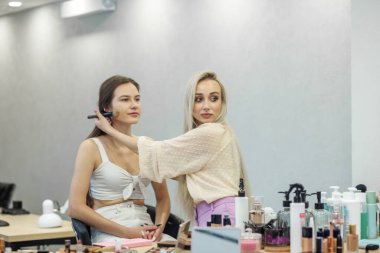 Makyaj fırçası. Yüze makyaj uygula. Samimi güzellik salonu. Cilt bakımı. Küçük bir iş. İki kadın. Düğün günü için hazırlık yapıyorum. Bir sürü kozmetik ürünü. Büyük ayna. Temelin rengini eşleştir.