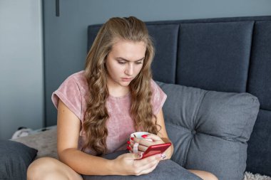 Genç bir kız yatakta oturur ve çay içer. Cep telefonu kullanıyor. Bir kadın akıllı telefon kullanarak sosyal ağlarda mesajlaşıyor..