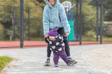 Kalın giysilere sarılmış küçük bir çocuk kaldırımlı bir yolda ilk adımlarını atıyor ve aile rehberliği parka gidiyor.