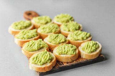 Çıtır ekmek dilimlerinde taze avokado püresi servis edilir, ahşap bir tahtada düzenlenir, aperatifler, aperatifler veya yemek servisi için idealdir..