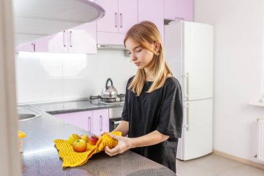 Siyah gömlekli genç kız mutfak tezgahında yeni yıkanmış elmaları kurutmak için sarı havlu kullanıyor..