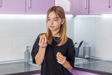 Siyah gömlekli genç kız ellerinde mandalina dilimlerine bakıyor. Evde taze ve sağlıklı bir şeyler yemeye hazırlanıyor..