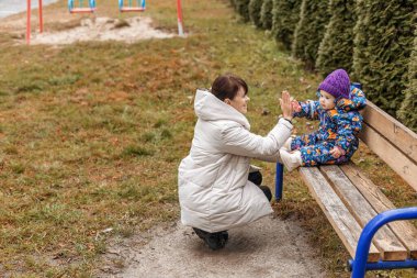 Annesi bir bankın yanına çömelir ve ona sıcak giyimli bir beşlik çakar. Hem de eğlenceli bir kış gezisinde..