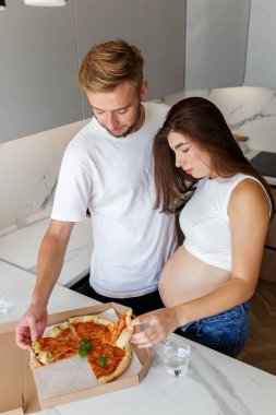 Genç çiftin evde pizzalarını paylaşmasını bekliyorum. Mutfakta hamilelik sırasında sevgi, birliktelik ve rahat bir yaşam tarzı gösteriyorlar..