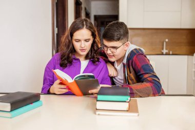 Mutfakta masada oturan iki genç, birlikte kitap okumaya ve çalışmaya odaklanmış, ödev ya da öğrenme üzerine işbirliği yapıyorlar..