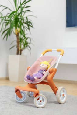 İçinde sevimli pelüş bir bebek olan renkli oyuncak bebek arabası, yumuşak halısı ve bitkisi olan parlak, modern bir oturma odasına yerleştirilmiş..