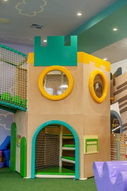 Kale temalı bir tırmanma kulesi, yuvarlak pencereleri, yastıklı zeminleri ve çocuklar için ağlı güvenlik özellikleri olan renkli bir oyun alanı..