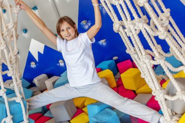 Genç kız gülümserken, renkli bir iç mekan tırmanma ve oyun alanında iki halat ağıyla tam bir bacak arasını ayırıyor..