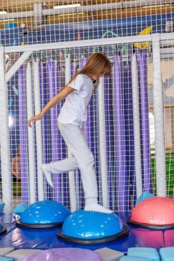 Genç kız, fiziksel oyun ve koordinasyon için tasarlanmış renkli bir kapalı etkinlik merkezinde yumuşak denge kubbelerinden dikkatle geçiyor..